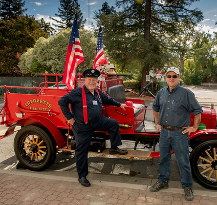 Two men standing in front of an antique red fire truck