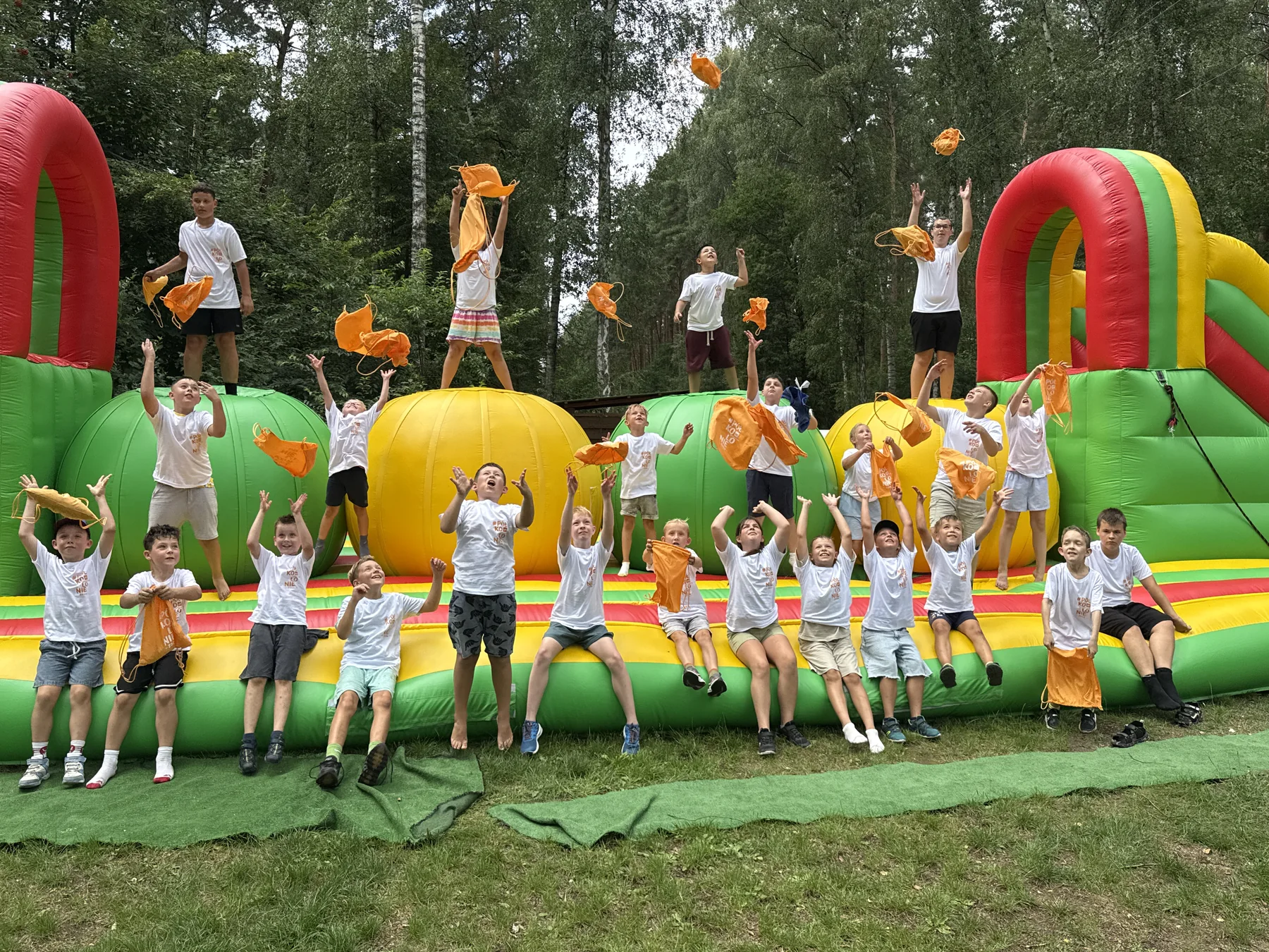 Dzieci podczas wspólnej zabawy na kolorowym dmuchańcu podrzucają pomarańczowe worki