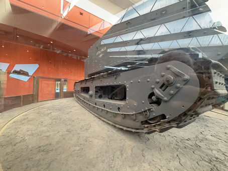 Museum exhibit of the gray tank Little Willie (1915), shown behind glass with orange walls and reflections.