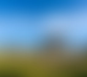 Ancient stone structures under a bright blue sky with scattered clouds, set in a grassy landscape with trees in the background.