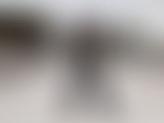 Man in fringed leather, tiger shirt, and studded pants poses with a large tusk on a dirt road. Trees, vans, and power lines in background.