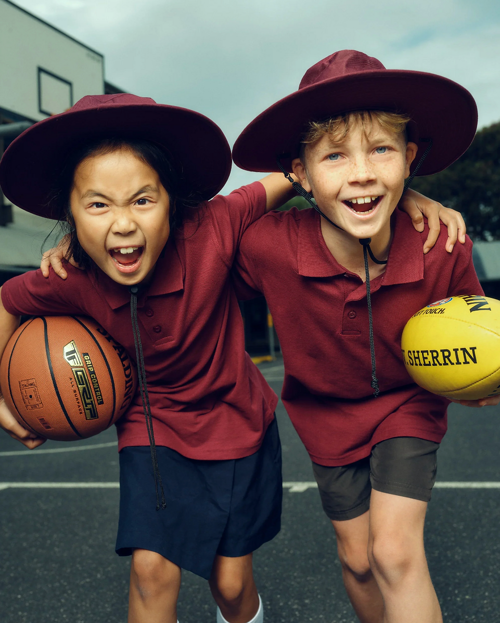 Excited kids in school uniforms with a basketball and football.