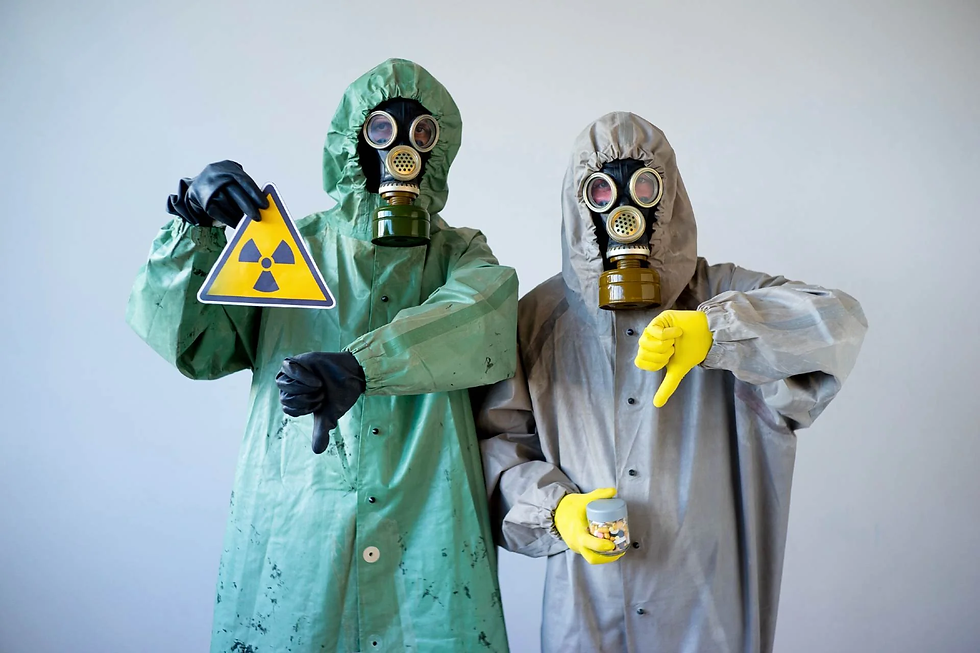 Two people in hazmat suits and gas masks give thumbs down, holding a radiation warning sign and a jar of pills. Gray backdrop.