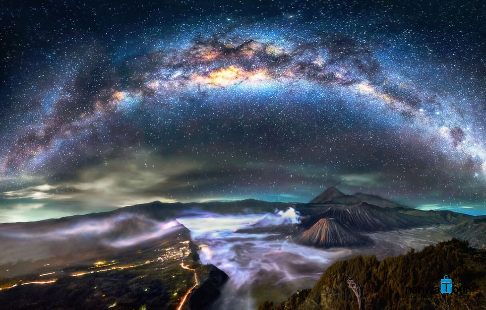 Starry night sky with Milky Way over Mount Bromo, surrounded by misty landscape. Bright and colorful cosmic view, creating a tranquil scene.