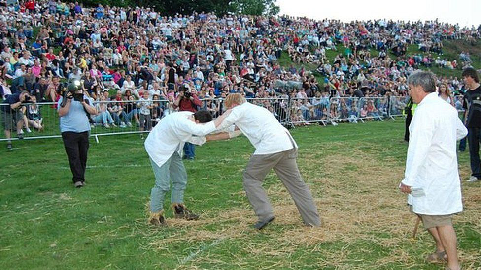 Two men in white coats hanging onto each other at the Shin Kicking competition in England
