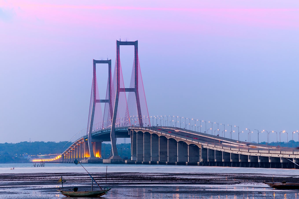 Large suspension bridge at sunset with pink and blue sky. Bridge lights are on above the water, creating a serene and calm atmosphere.