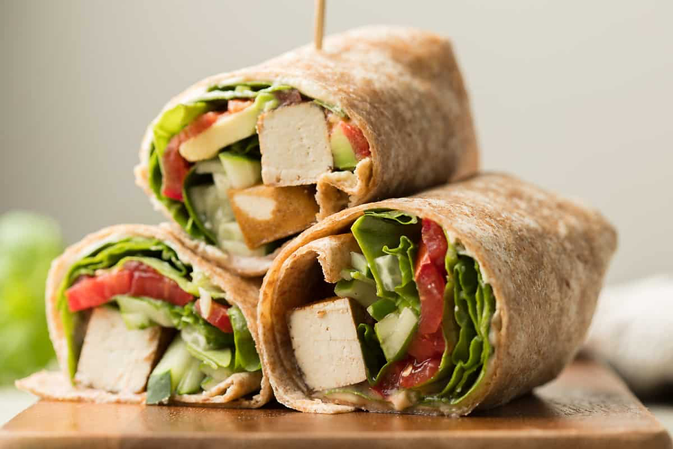 Three wraps stacked on a wooden board, filled with tofu, lettuce, tomato, and cucumber. Fresh and colorful, creating an appetizing look.