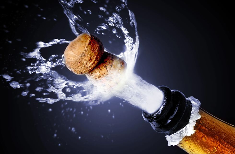 Cork popping from a champagne bottle, splashing liquid, against a dark background. The image conveys celebration and excitement.