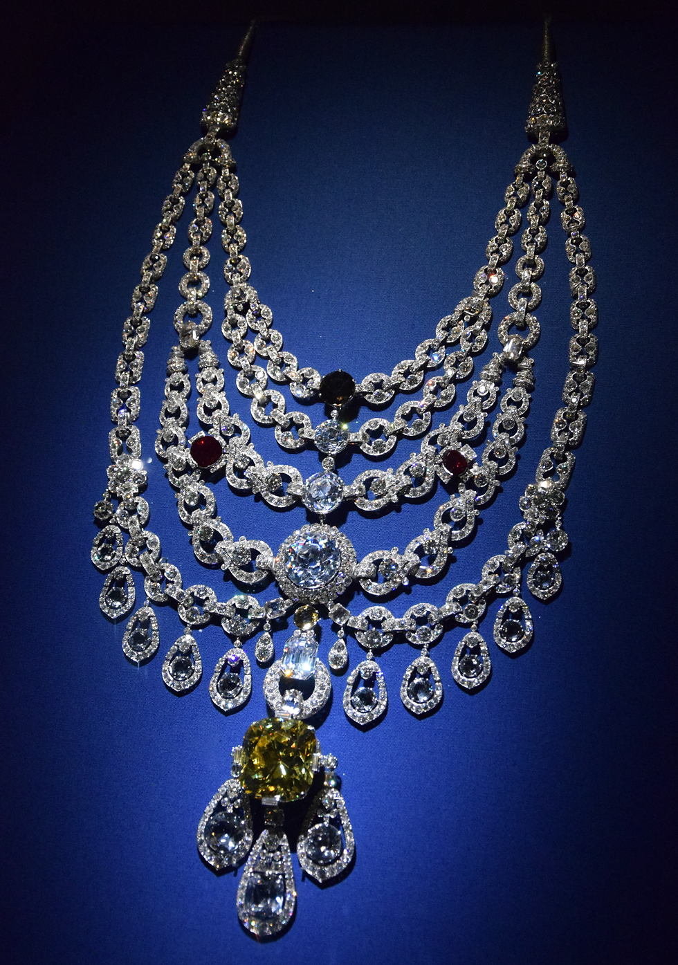 Sparkling Cartier diamond necklace with layered teardrop pendants and a large yellow center gem displayed on deep blue fabric.
