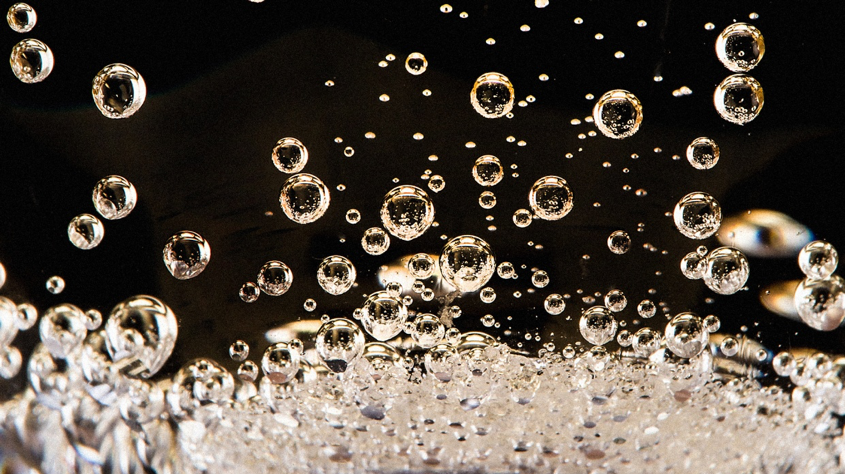 Bubbles rising in sparkling water against a black background, creating a lively and dynamic scene with bright reflections.
