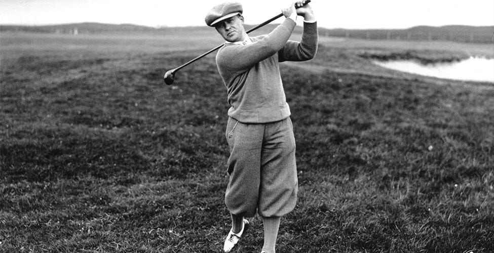 Golfer - Bobby Jones - swings on a grassy course, wearing vintage attire and cap. Overcast sky, body mid-swing. B/W image with a serene mood.