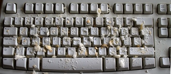 Crumb-covered keyboard with white keys, crumbs scattered throughout. Messy and cluttered appearance indicates recent snack accident.