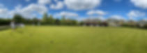 Lawn bowling green with clubhouse and blue sky with fluffy clouds, people playing lawn bowls wearing white clothes