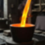 Copper-colored hot molten metal being poured into a crucible. The setting is an industrial