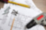 Blueprints, screws, measuring tape, and a power drill on a wooden surface, symbolizing planning and compliance in commercial construction projects.