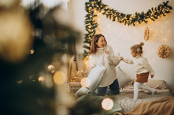 Mother and Daughter Playfully Enjoying Time Together on a Bed Surrounded by Christmas Decorations, Symbolizing a Healthy and Joyful Indoor Environment During the Holiday Season in Central Florida.