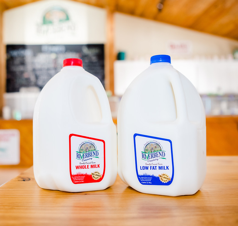 A gallon of whole and low fat milk sitting on a wooden table inside Riverbend Creamery.