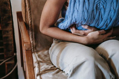 Lady in a blue jumper sitting on a chair holding her stomach