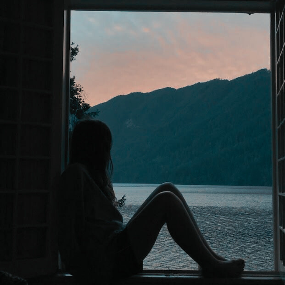 Person sitting by a calm lake overlooking mountains at dusk