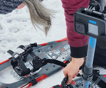 A woman, my mom, Genevieve Turcotte, binding up her snowshoes with a gopro camera attached to her walking pole.