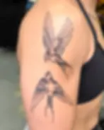Tattoo of swallows in flight, flying near one another in a fine line style, black and grey ink