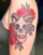Custom drawn tattoo showing a skull with horns surrounded by bright red flowers, in the NeoTraditonal style