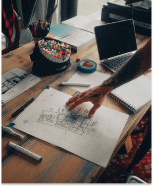 Hand placed over a sketched idea that is on top of a workstation.