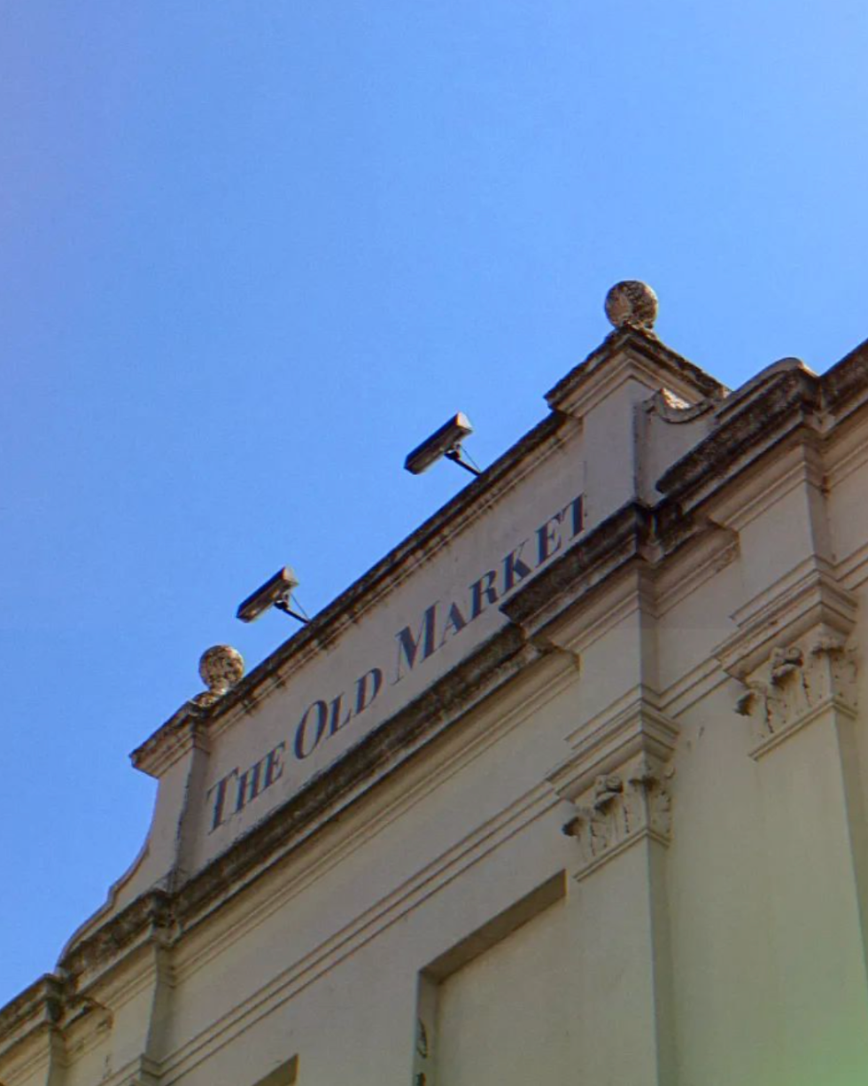 Facade of The Old Market building against a clear blue sky, with rooftop lights and ornate trim.