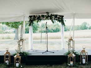 A wedding stage, with a microphone in the middle, and an arch with white and pink flowers around it.