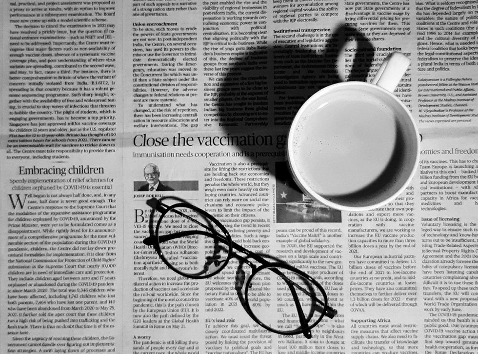 A close-up of a black and white newspaper, with a pair of glasses and a cup of coffee sitting on the open page.