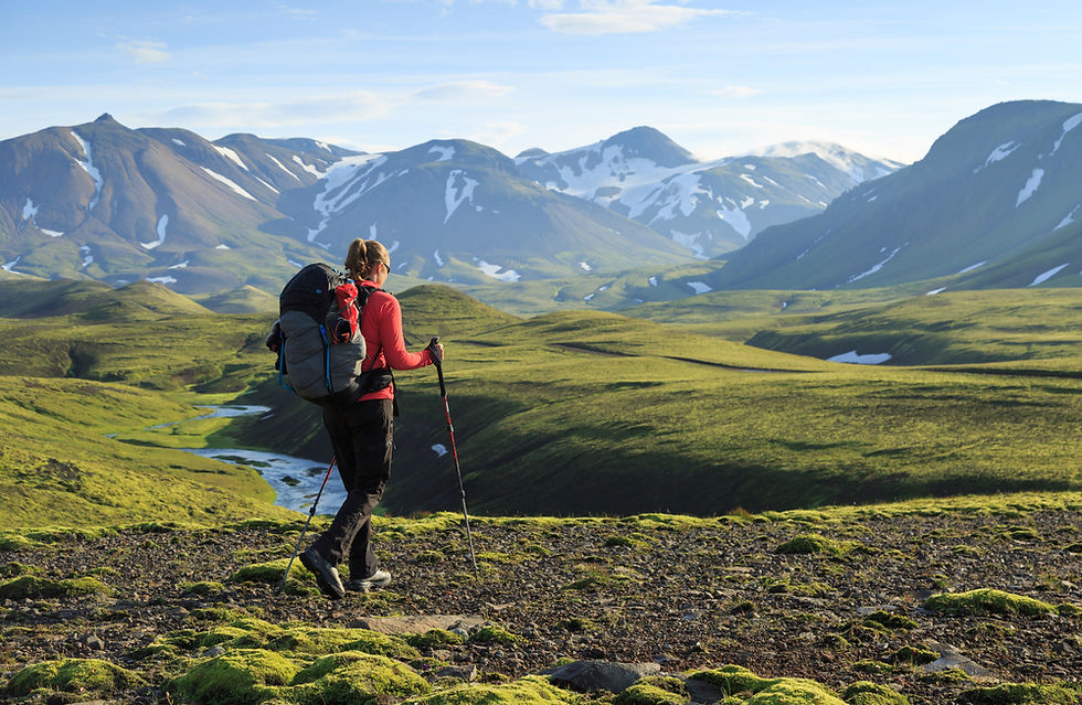 Female hiker heading across a trail. Green landscape and snow on mountains in distance. Hiking in Iceland.