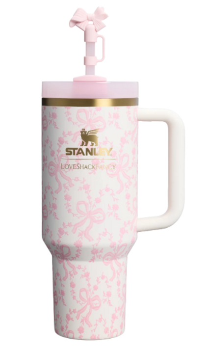 Pink and white floral-patterned mug with "STANLEY" and "LOVESHACKFANCY" text. Gold rim, bow detail on lid, evokes elegance.