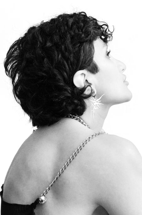 Profile portrait with short curly hair, gaze upward, spiked star earring, thin metal chain draped over bare back – Photography from the series 'Transgression durch Hoffnung' by Alfred Stoll, 2025–2026. Metamodern Art; Exhibition kultur.lokal.fürth; Metamodernism; Metamodern Grotesk.
