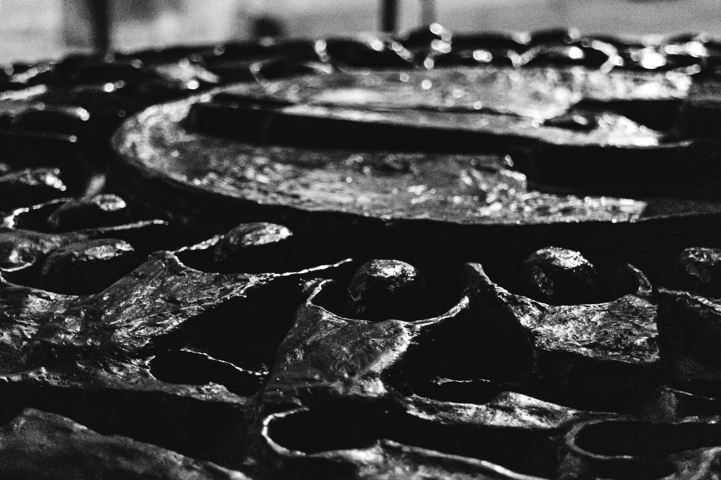 Close-up of textured metallic surface, possibly a manhole cover, strong highlights and deep shadows – Photography from the series 'Transgression durch Hoffnung' by Alfred Stoll, 2025–2026. Metamodern Art; Exhibition kultur.lokal.fürth; Metamodernism; Metamodern Grotesk.