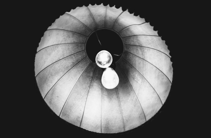 View into a circular lampshade with two light bulbs in the center, pleated texture – Photography from the series 'Transgression durch Hoffnung' by Alfred Stoll, 2025–2026. Metamodern Art; Exhibition kultur.lokal.fürth; Metamodernism; Metamodern Grotesk.