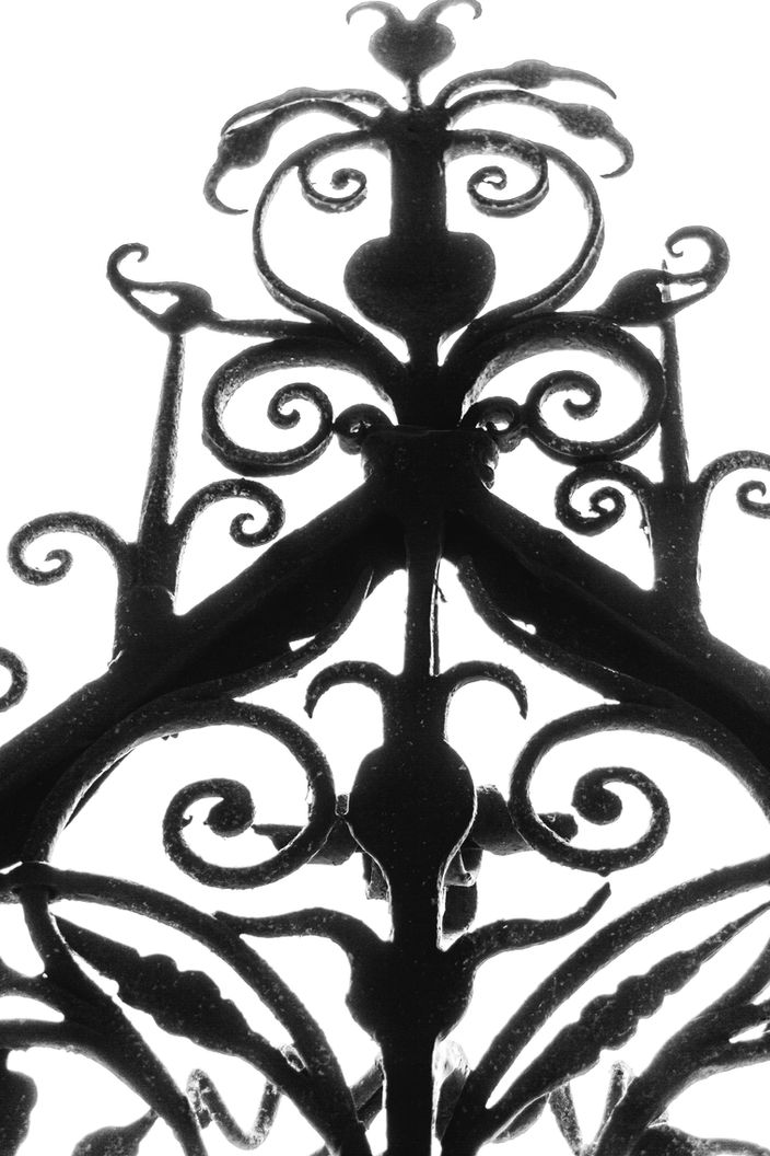 Ornate wrought-iron gate with scrolls, curves and heart-like shapes silhouetted against bright background – Photography from the series 'Transgression durch Hoffnung' by Alfred Stoll, 2025–2026. Metamodern Art; Exhibition kultur.lokal.fürth; Metamodernism; Metamodern Grotesk.