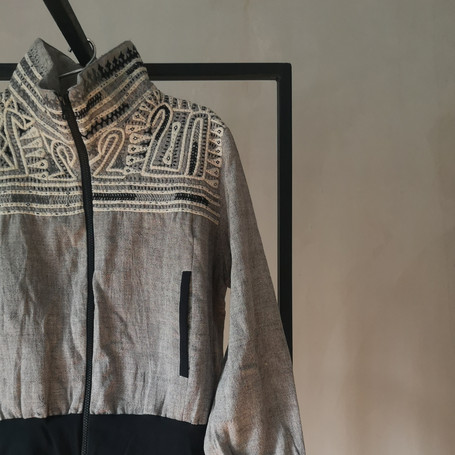 a grey jacket with colorful hand-embroideries in organic cotton on a hanger