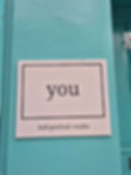 Sign on a turquoise wall reads "you" and "Self-portrait studio." Number "2" partly visible on the door, creating a creative, inviting vibe.