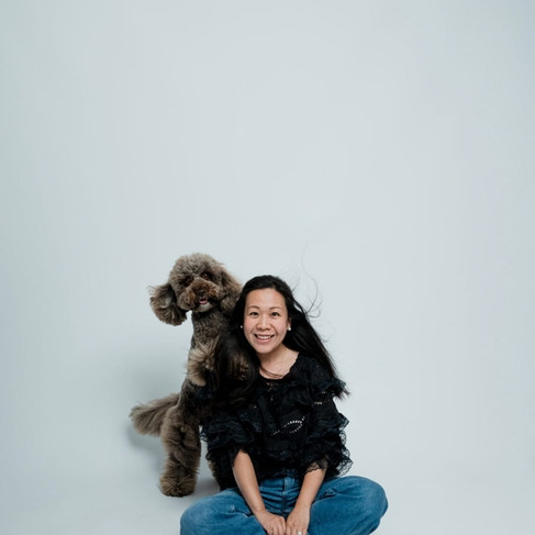 A woman sits on the floor with a fluffy brown dog behind her. Its front paws are on her shoulders