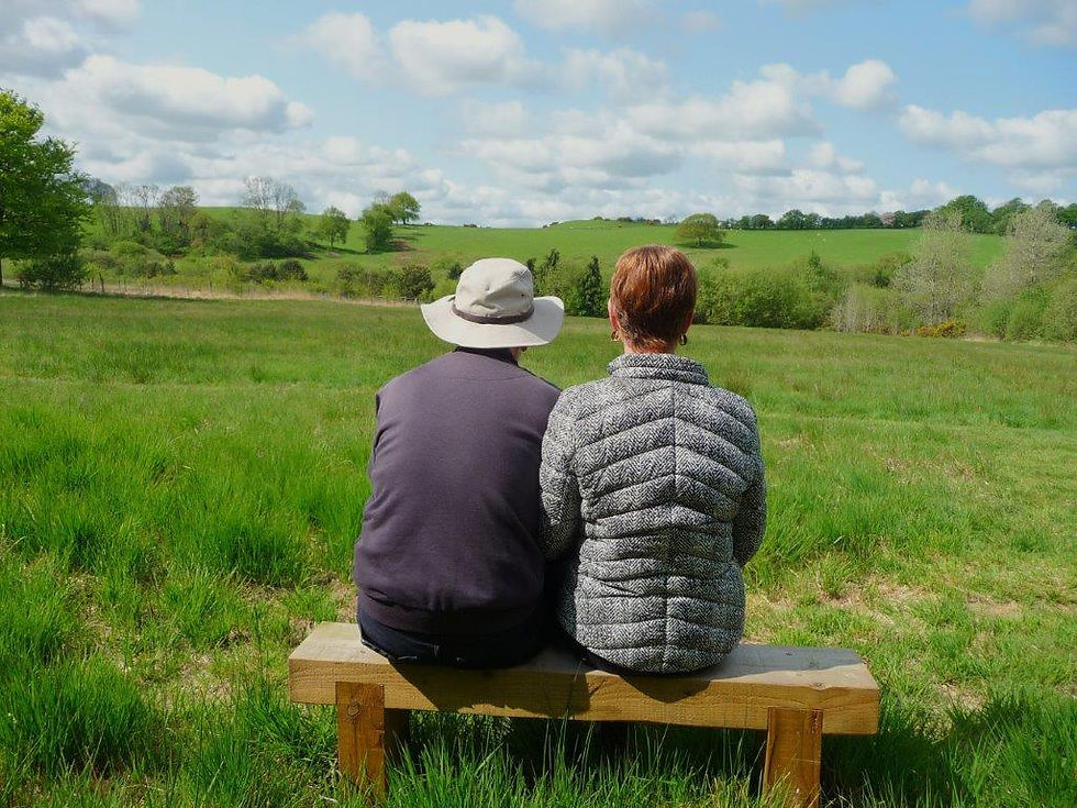A couple sit on a bench in a field taking in the view