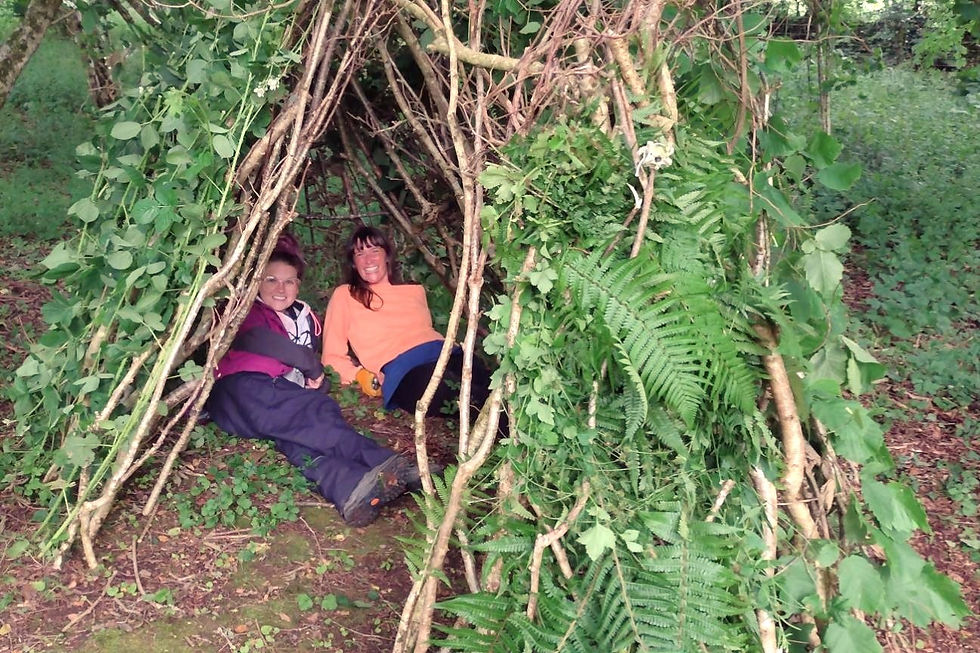 Two women lie in a shelter of sticks and leaves