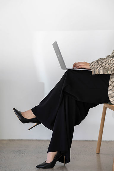 Close-up of a woman in black pants and heels working on a laptop, legs crossed, focused on her task.