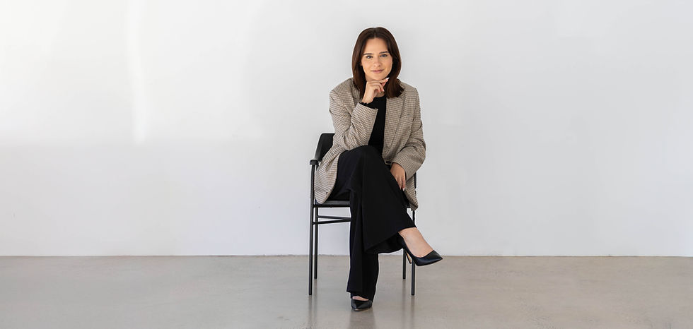 A confident woman in a beige blazer holds a laptop while standing against a white background.