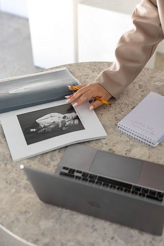 Close-up of hands writing in a notebook next to a laptop and magazine, planning content.