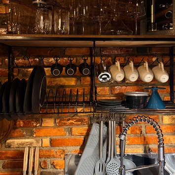 Detalhe da cozinha totalmente equipada na cabana de montanha, mostrando prateleiras de metal com louças completas, xícaras e utensílios organizados.