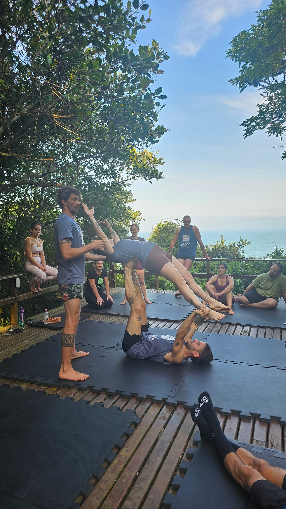 Participantes iniciantes praticam Acroyoga em grupo durante retiro próximo à praia 