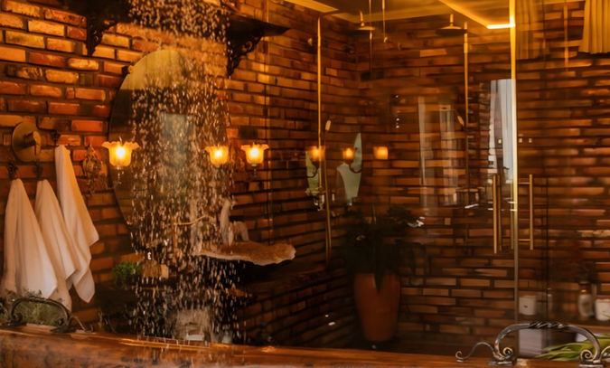 Banheiro de design rústico chic exclusivo da cabana, com paredes de tijolo aparente, banheira de imersão esculpida em tronco de árvore maciço , chuveiros duplos à gás, e iluminação acolhedora