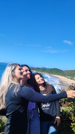 Três participantes abraçados em mirante com o mar de Balneário Camboriú ao fundo