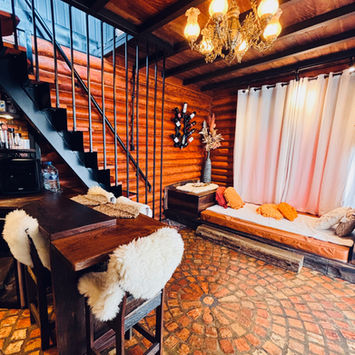 Sala de estar e jantar rústica com piso de tijolos, mesa de madeira maciça, cadeiras com pelegos macios e escada metálica de acesso ao mezanino.