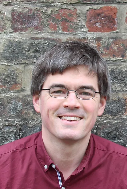 Huw Daniel headshot, against a brick background.